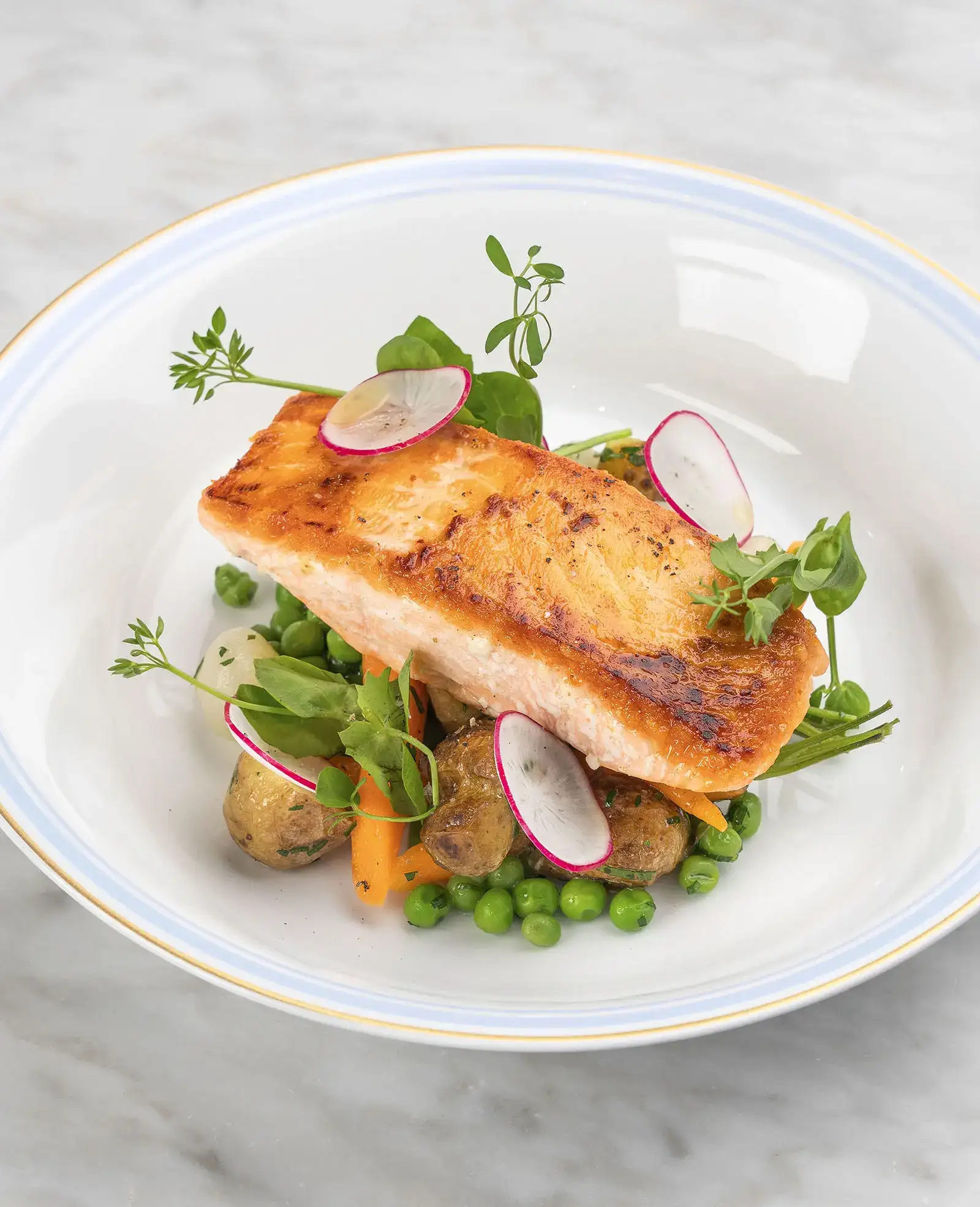 A plate of grilled salmon with baby potatoes and vegetables.