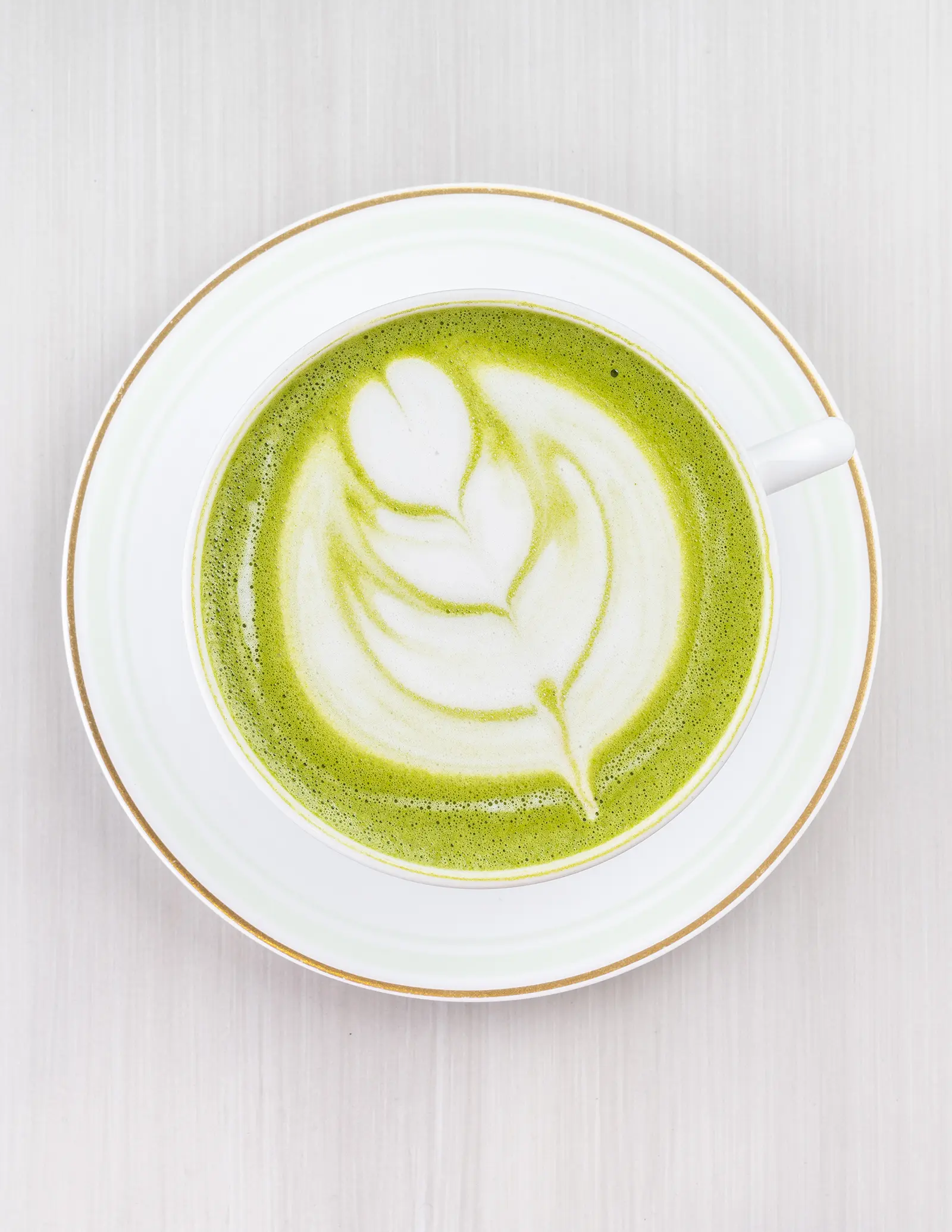 A cup of hot green matcha latte with foam art.