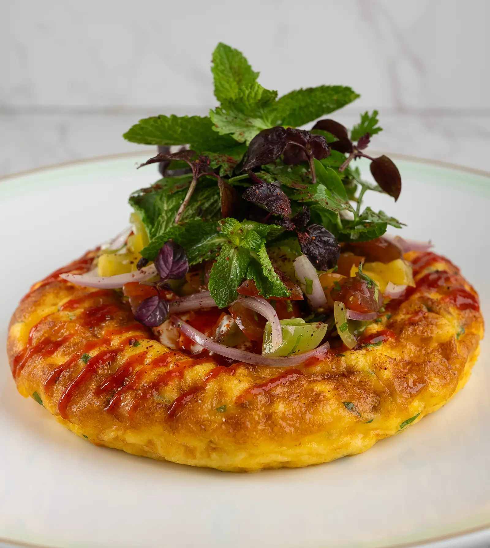 A colorful omelet with cherry tomatoes, red onion, a side of garlicky yogurt, and chili sauce.