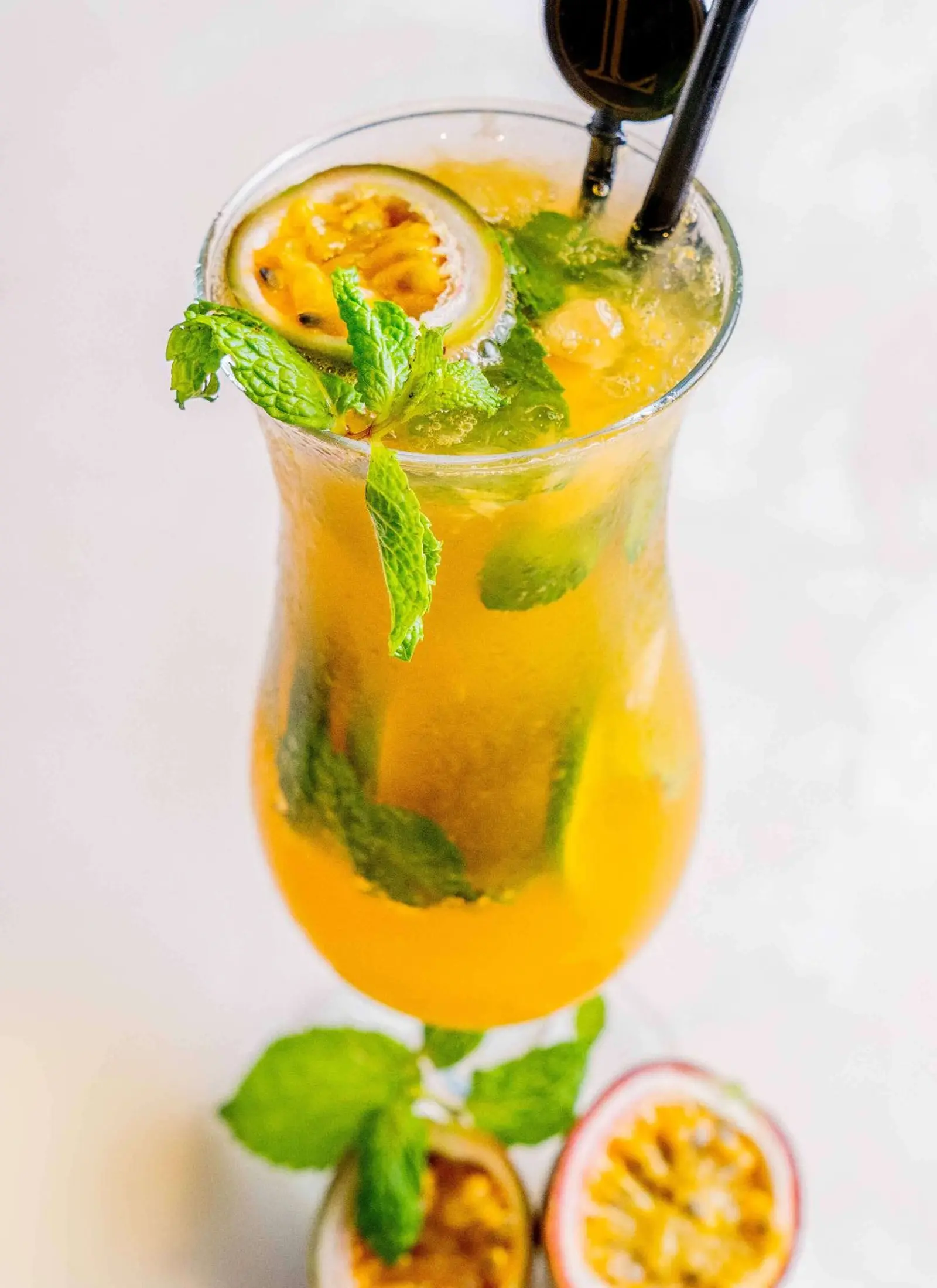 A glass of a tropical drink with passion fruit and a ginger garnish.