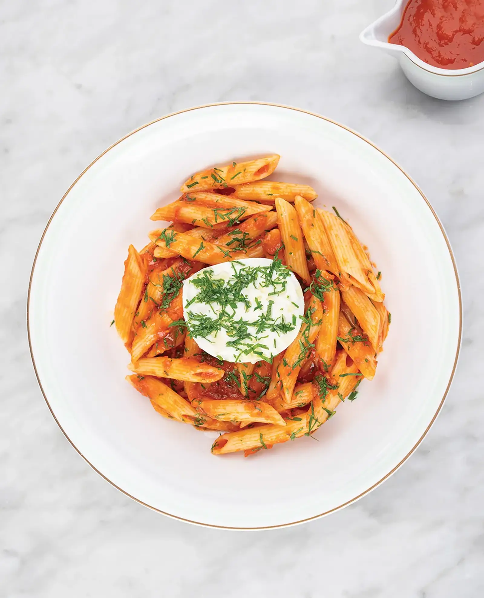 A bowl of penne pasta with a red sauce, topped with cheese and basil.