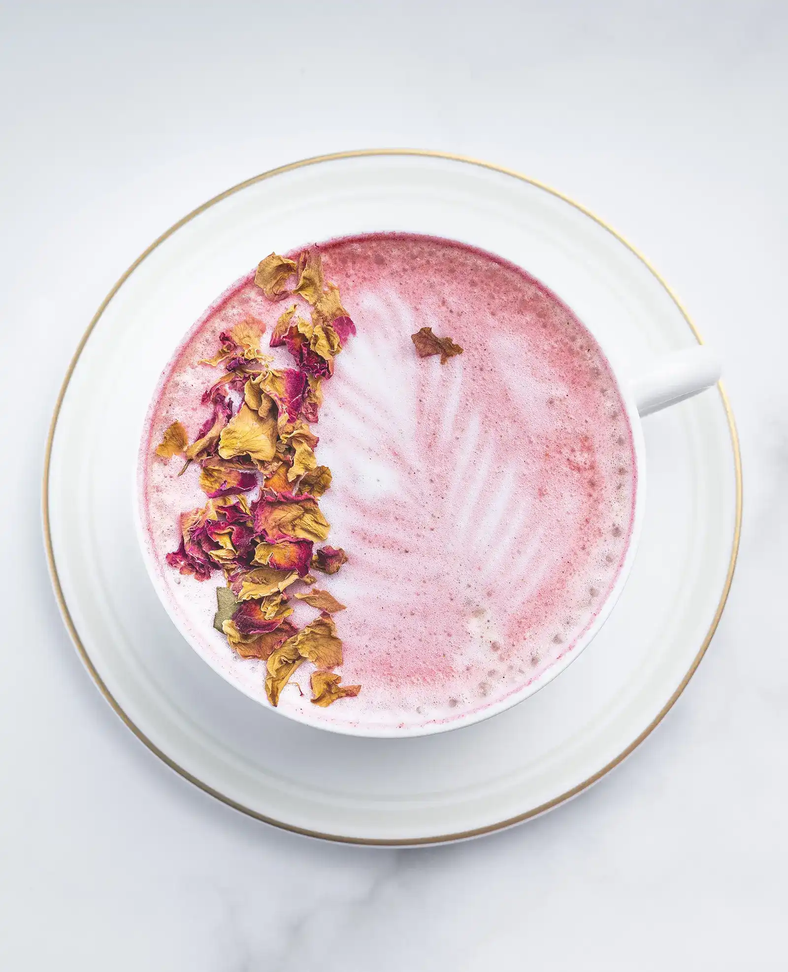 A cup of pink rose latte with dry rose petals on top.