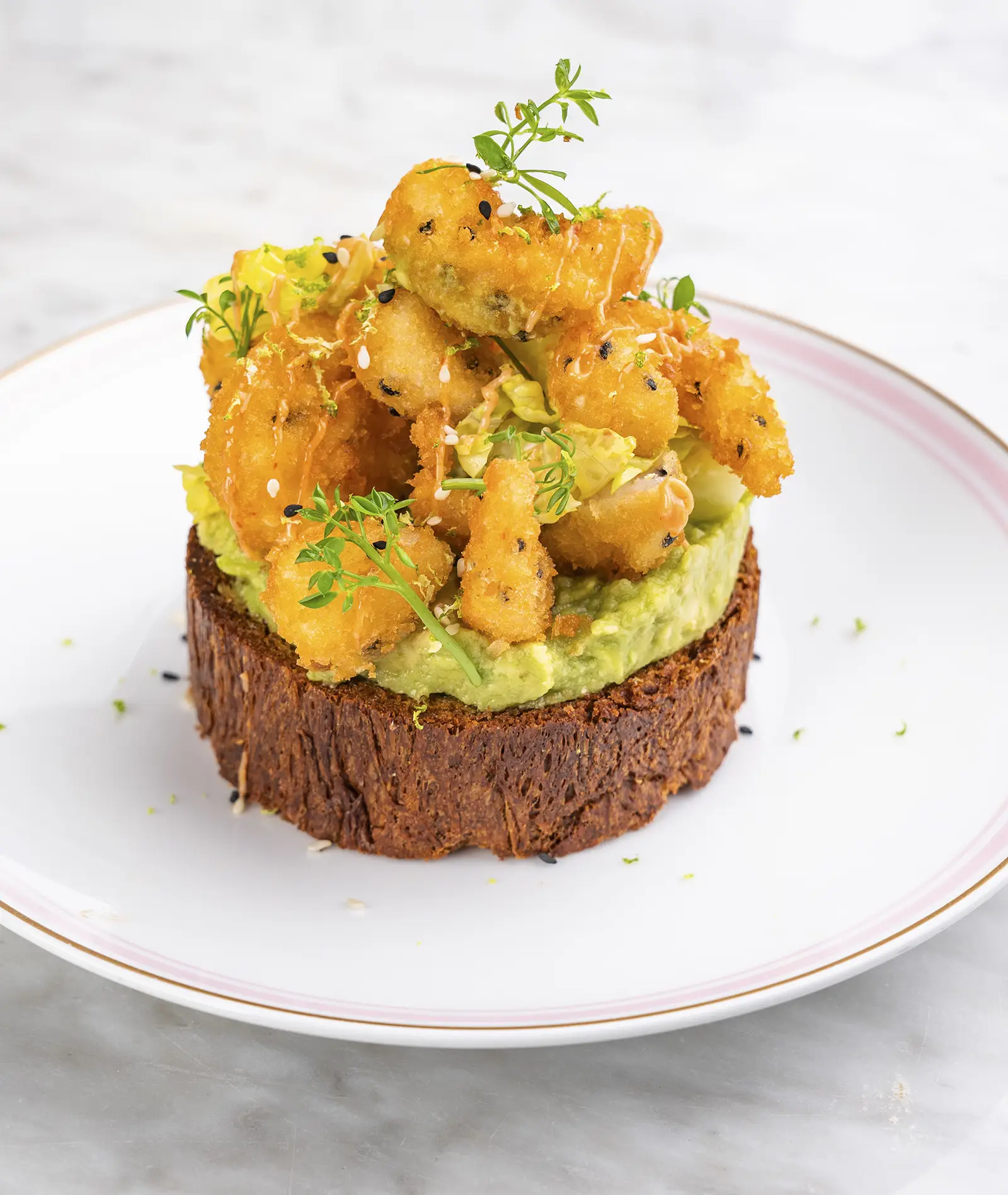 A brioche toast topped with avocado mash and breaded shrimp.