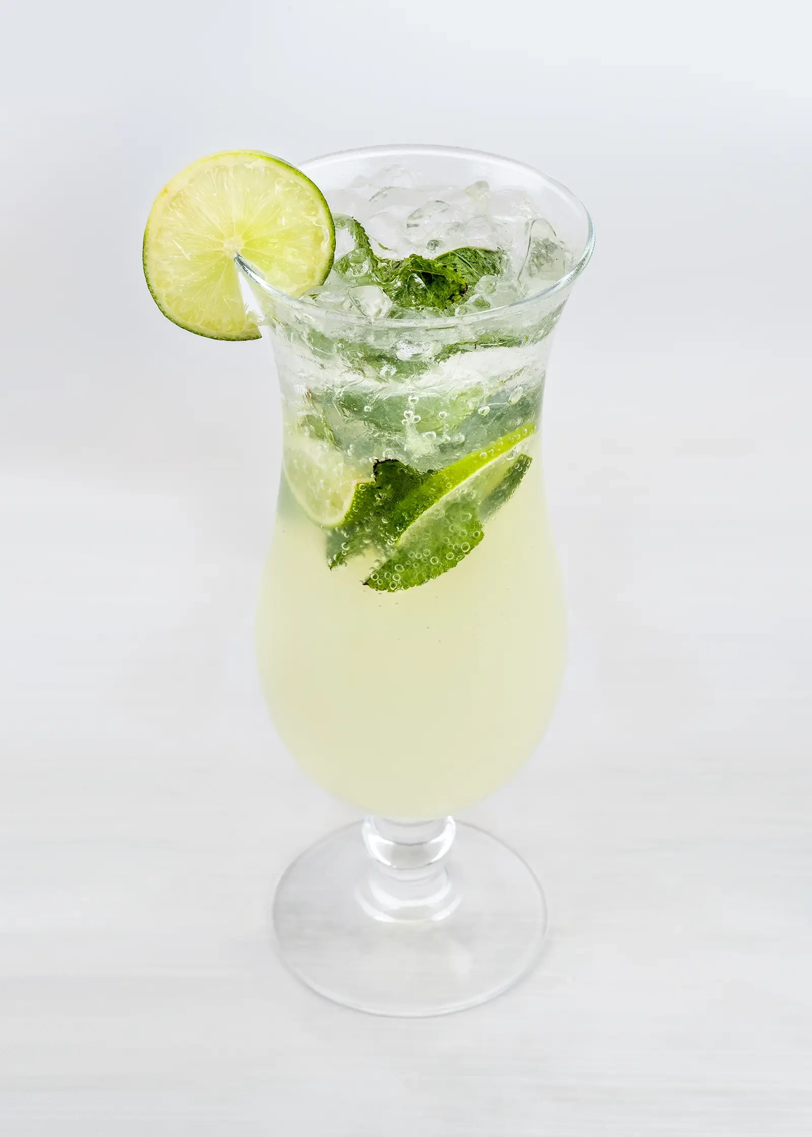 A tall glass of a green mojito with mint leaves and lime wedges.