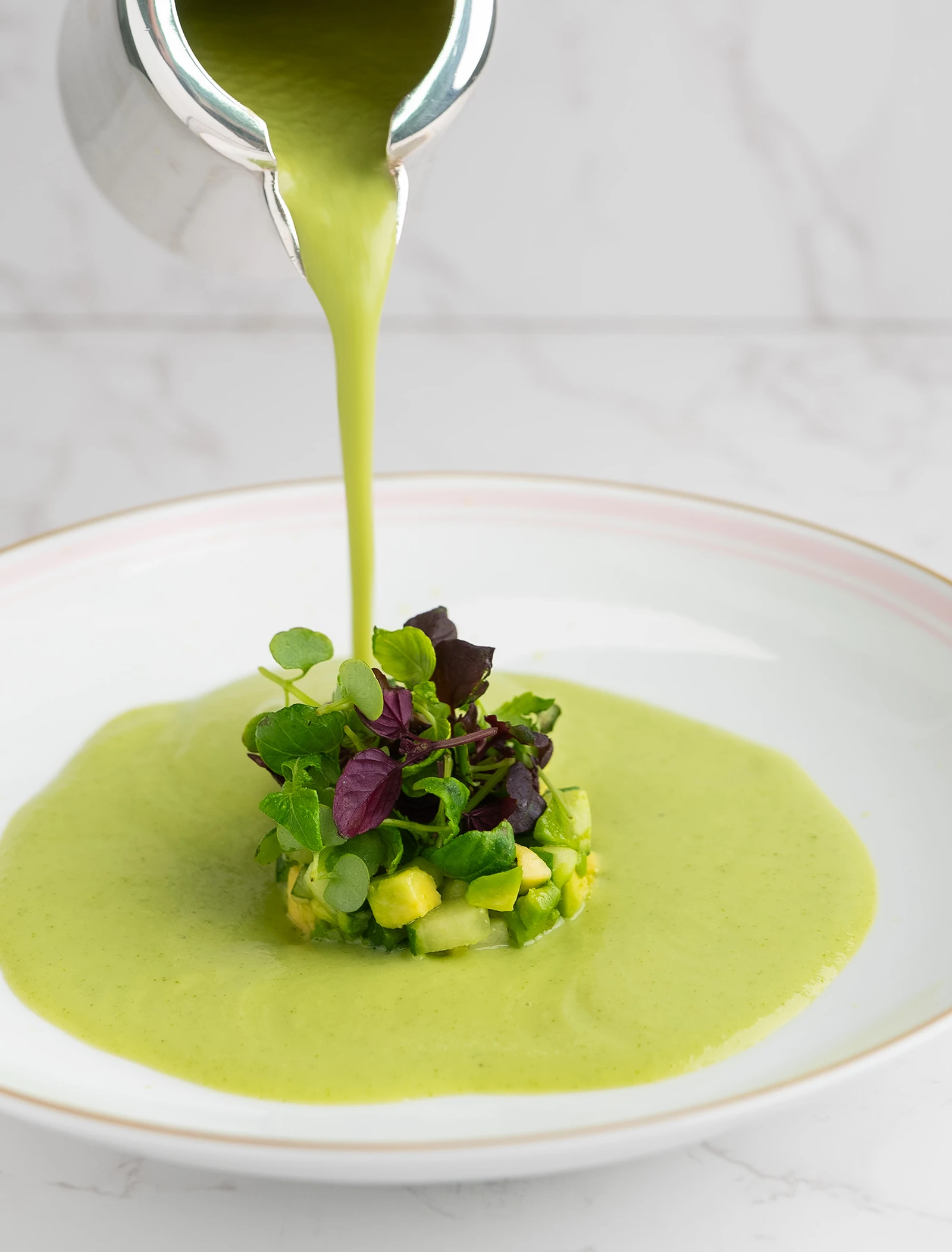 A bowl of green gazpacho with a garnish of herbs.