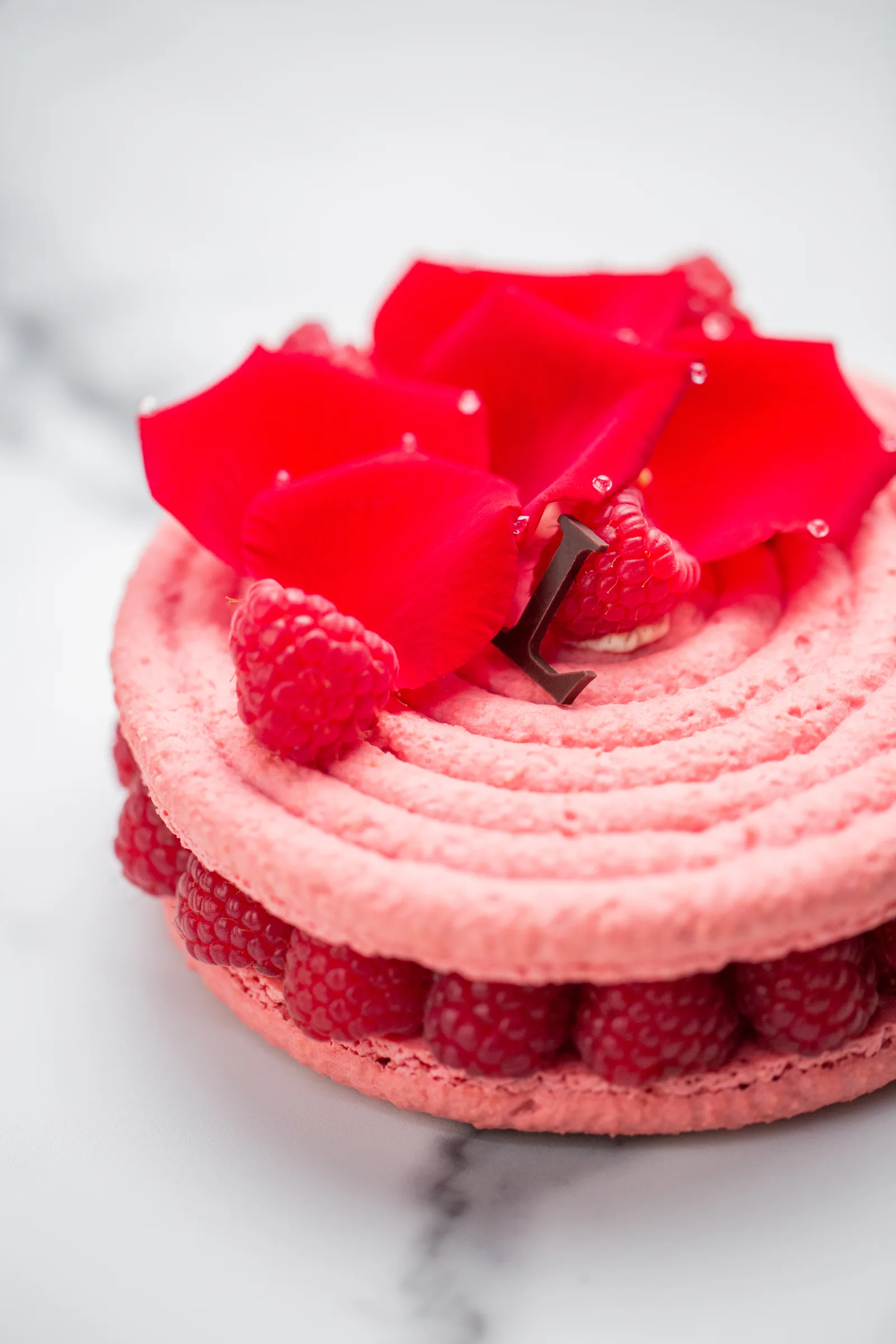 A delicate pink pastry with rose petals, fresh raspberries, and lychees.
