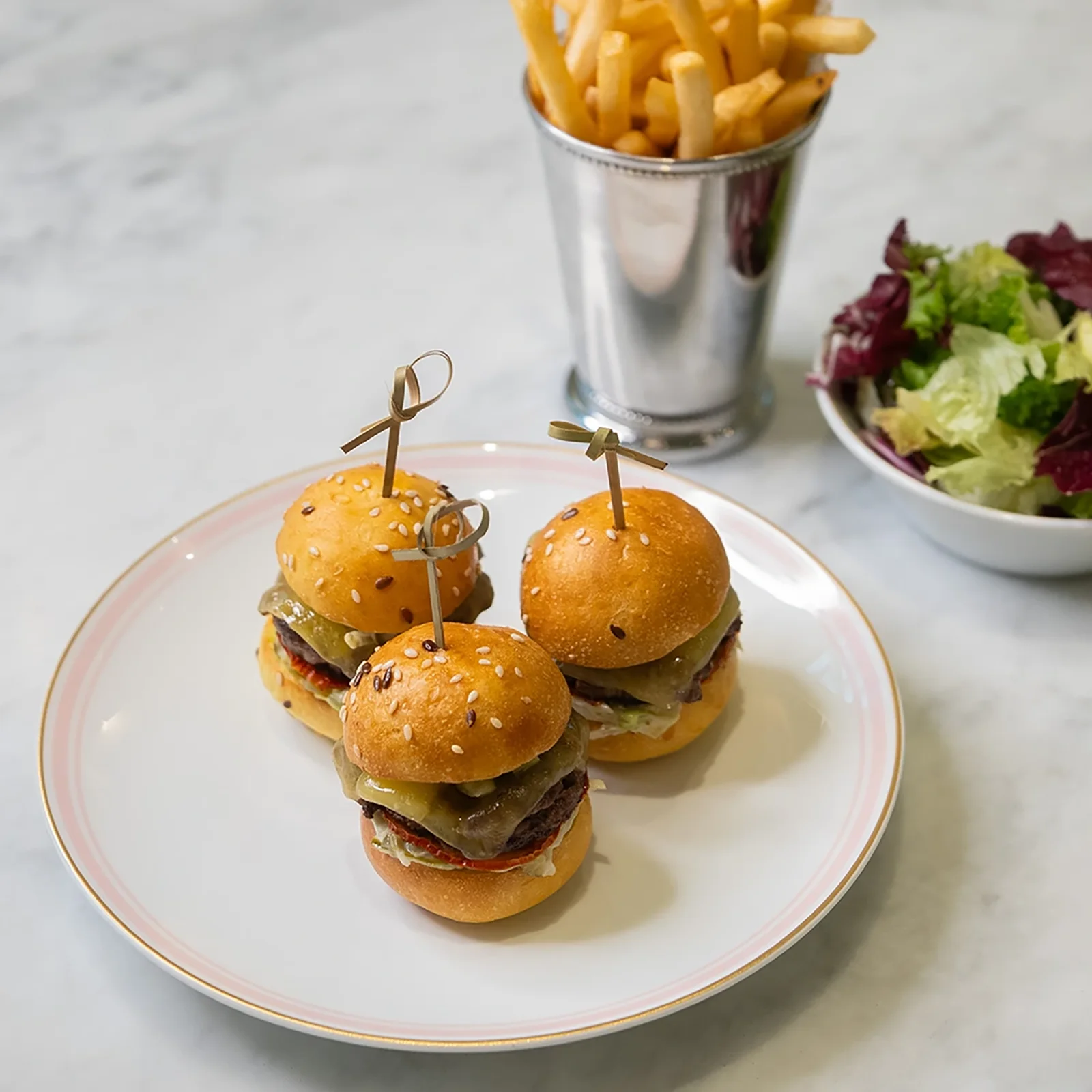 Two small beef sliders on potato buns served with fries and salad.