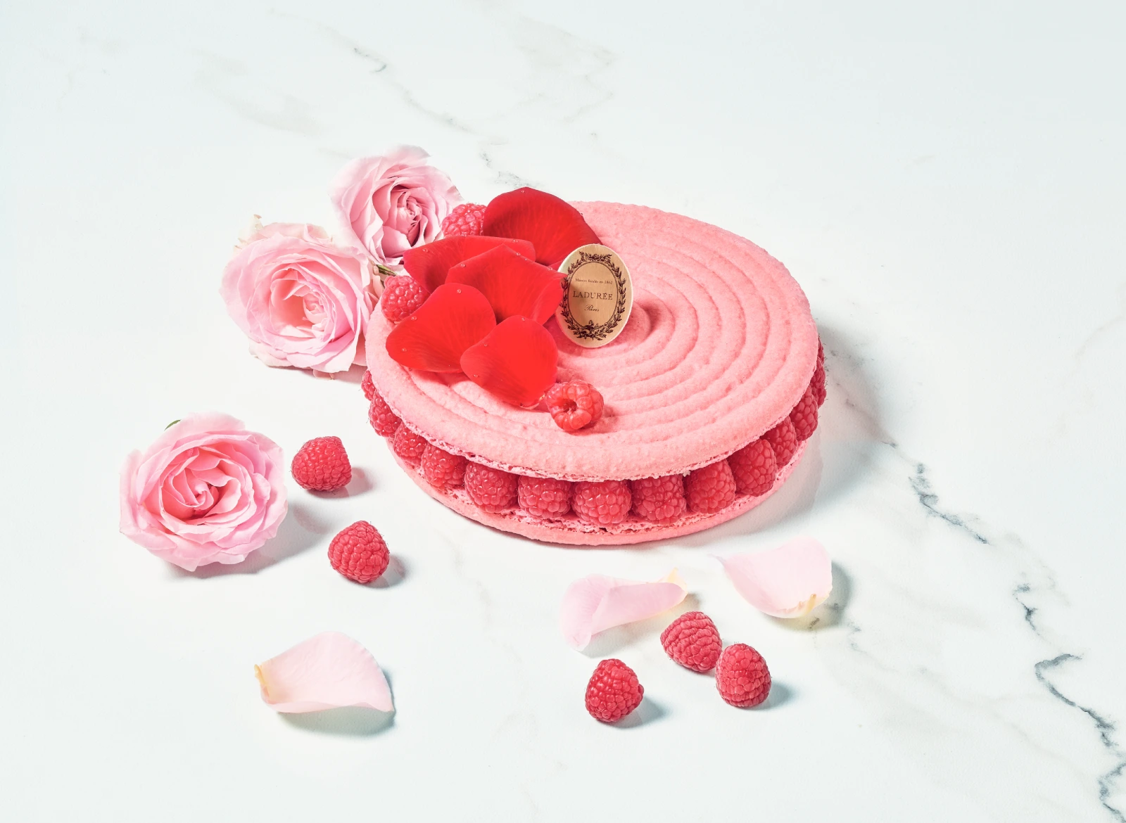 A delicate pink pastry with rose petals, fresh raspberries, and lychees.
