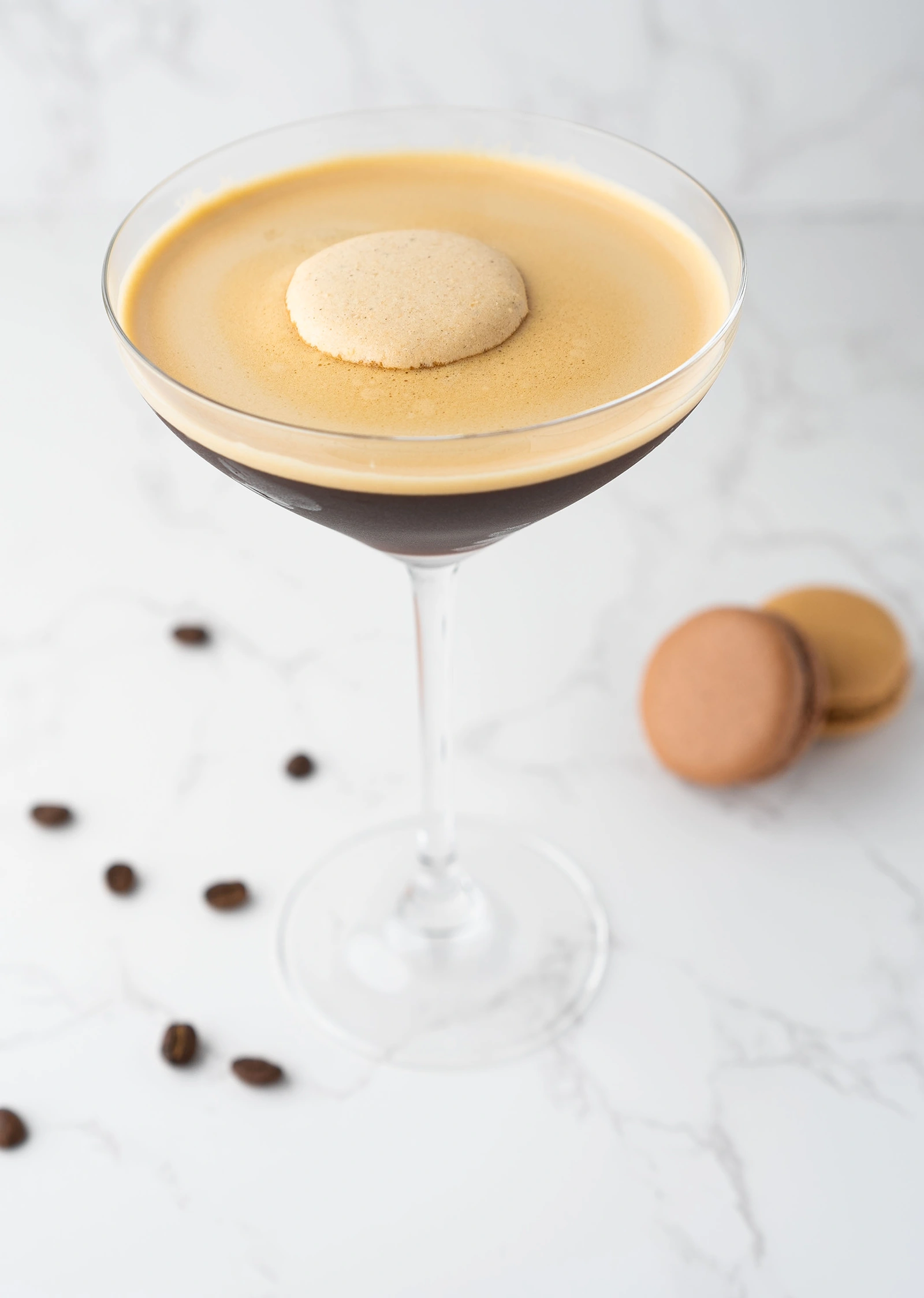 A martini glass with a coffee-colored drink and a macaron on the rim.