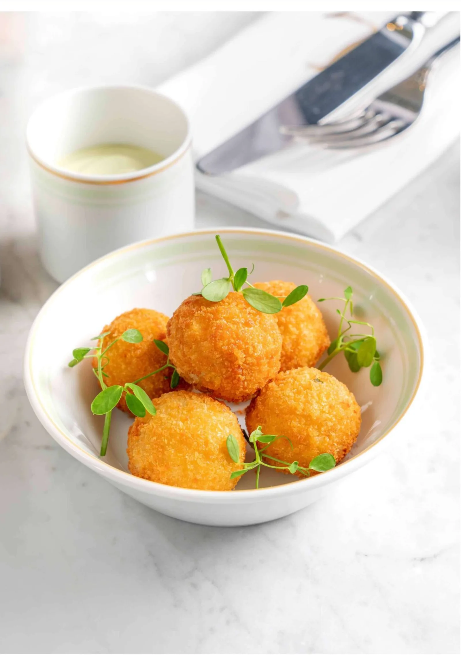 Golden-brown arancini (fried rice balls) served with a side of tomato sauce.