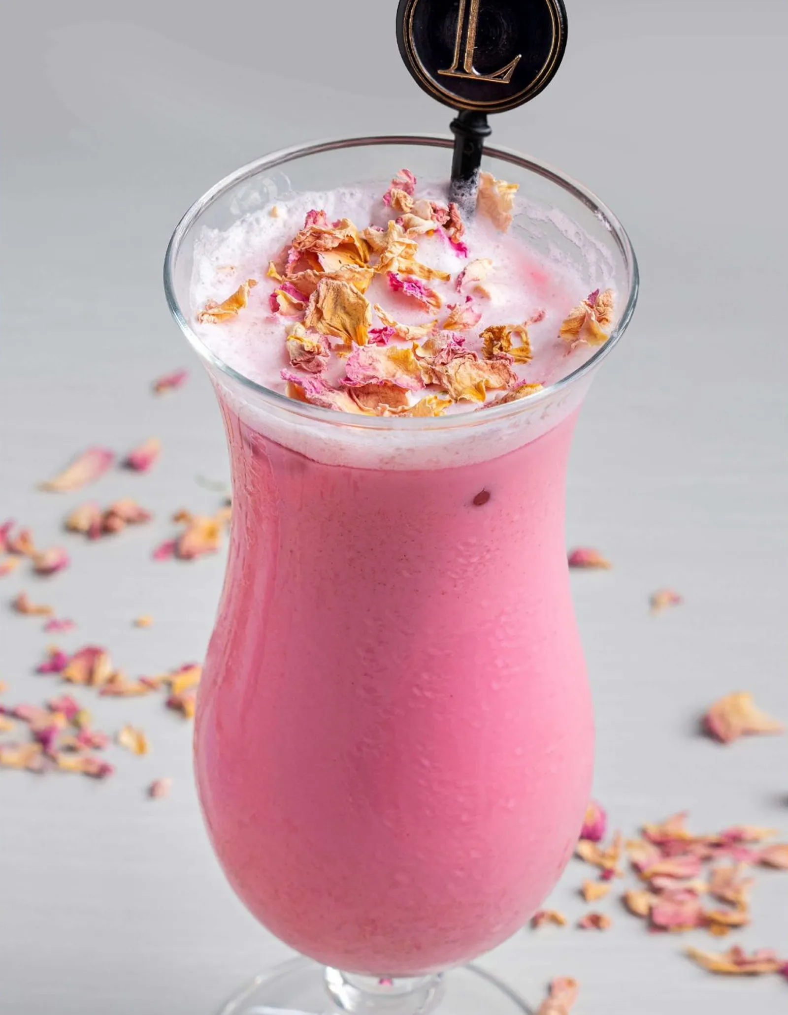 A tall glass of an iced pink latte with a straw.