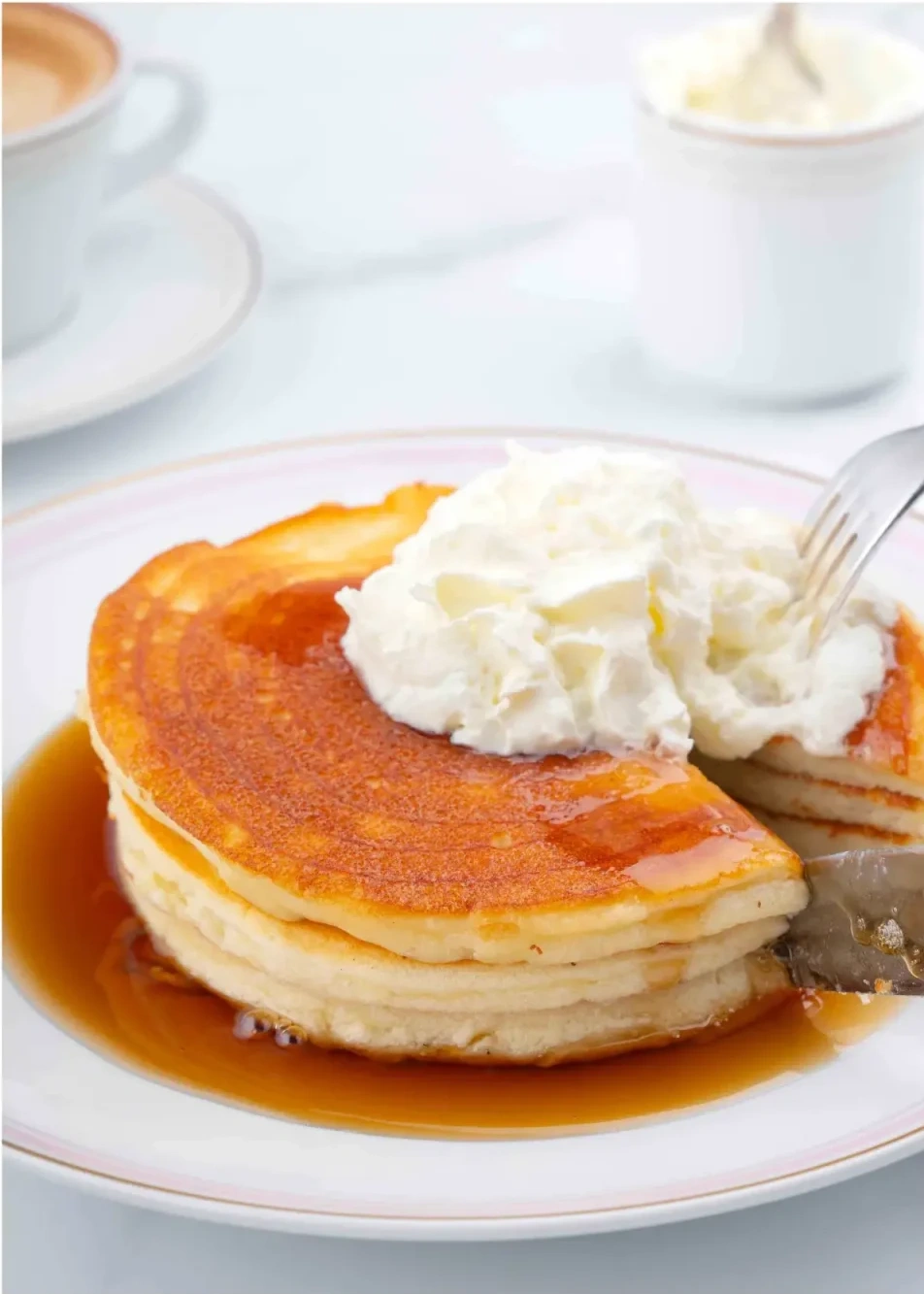 A stack of pancakes topped with a generous dollop of Chantilly cream and chocolate sauce.